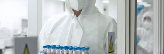 Person in PPE carrying tray of test tubes